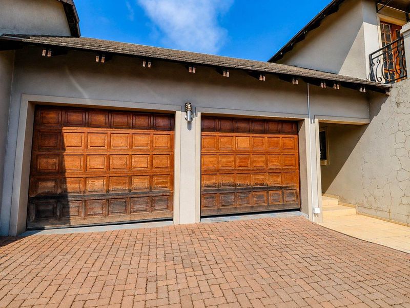 Double garage with wooden doors and paved driveway, featuring exterior wall lighting and tiled entrance steps to the main residence.