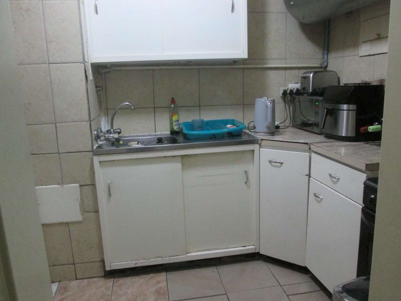 A compact, dated kitchen featuring built-in cabinetry, a stainless steel sink, and tiled finishes, offering potential for modernization and renovation.