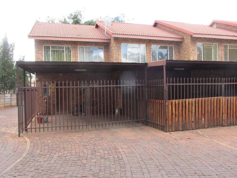 Front elevation of a face-brick apartment unit featuring a covered carport, paved driveway, and secure metal gate entrance.