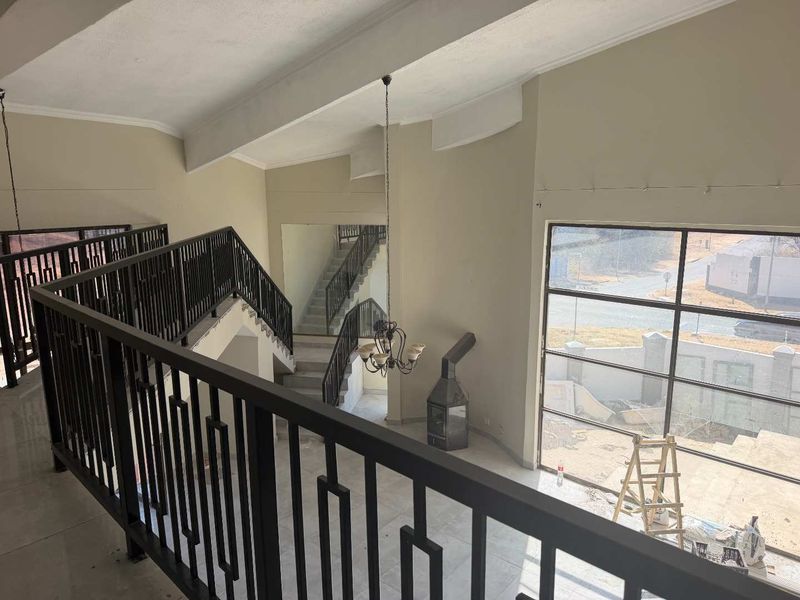 Spacious double-volume living area featuring a metal staircase, large windows, and a freestanding fireplace, currently in an unfinished state.