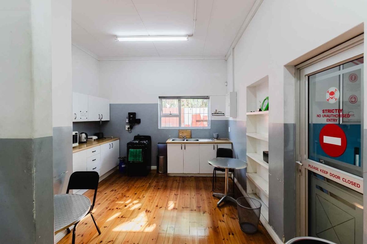 Functional kitchen area featuring white cabinetry, stainless steel sink, and polished wooden flooring, providing a practical space for staff or utility use.