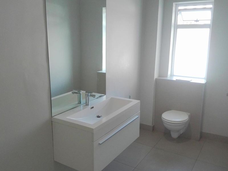 A modern, minimalist bathroom featuring a wall-mounted vanity with basin, wall-hung toilet, and neutral tiled flooring.