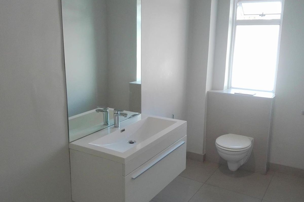 A modern, minimalist bathroom featuring a wall-mounted vanity with basin, wall-hung toilet, and neutral tiled flooring.