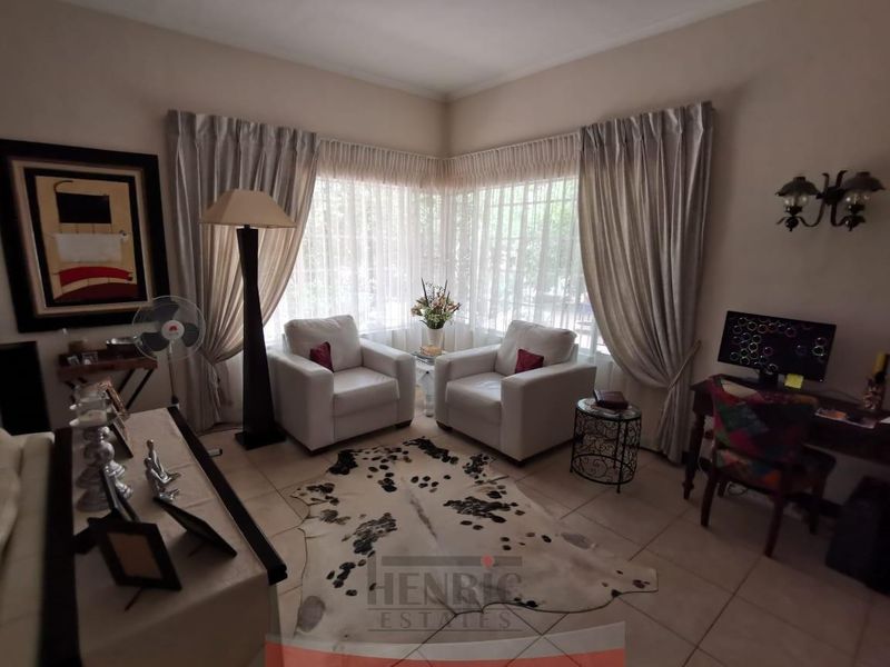 A comfortable living room featuring tiled flooring and large corner windows with installed curtain tracks, providing ample natural light.