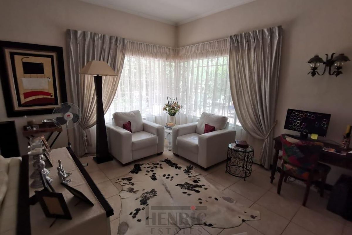 A comfortable living room featuring tiled flooring and large corner windows with installed curtain tracks, providing ample natural light.