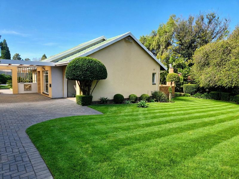 A well-maintained front exterior view featuring a paved driveway, attached carport, and a neatly manicured lawn with established garden landscaping.