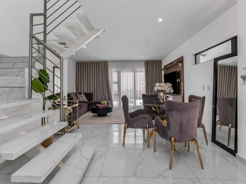 Modern open-plan living and dining area featuring sleek marble-look floor tiles, a contemporary staircase with stainless steel railing, and direct access to the patio.