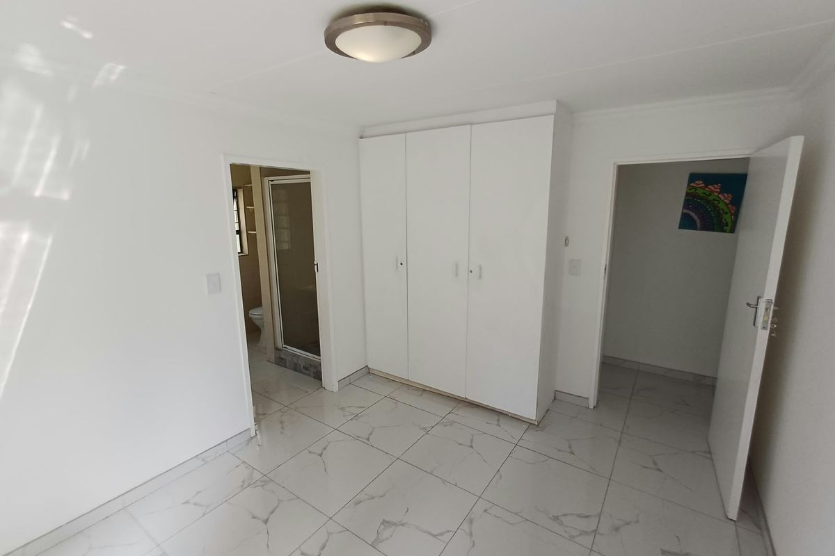 A clean, empty bedroom featuring modern white marble-look floor tiles, built-in cupboards, and direct access to an en-suite bathroom.