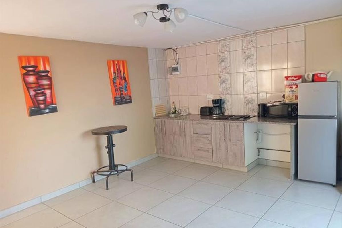 A functional kitchen area featuring laminate cabinetry, granite countertops, and tiled backsplash, with neutral ceramic flooring throughout.