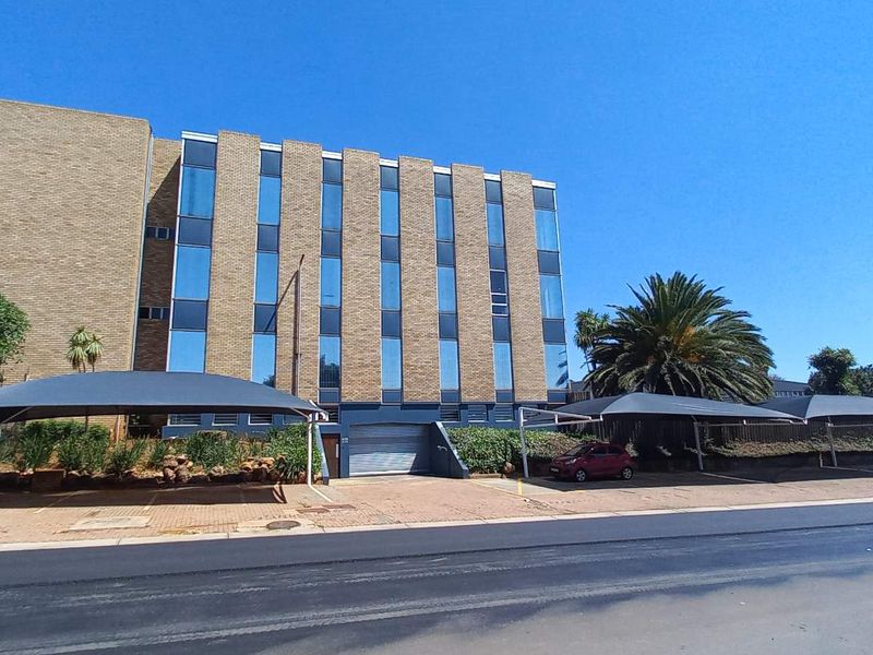 Front exterior view of a multi-story office building featuring a brick facade, large glass windows, and multiple covered parking bays.