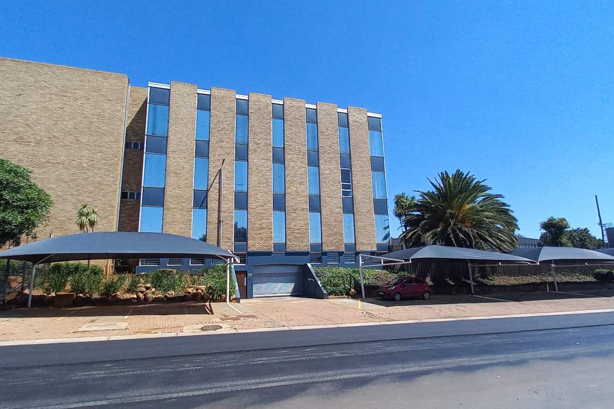 Front exterior view of a multi-story office building featuring a brick facade, large glass windows, and multiple covered parking bays.