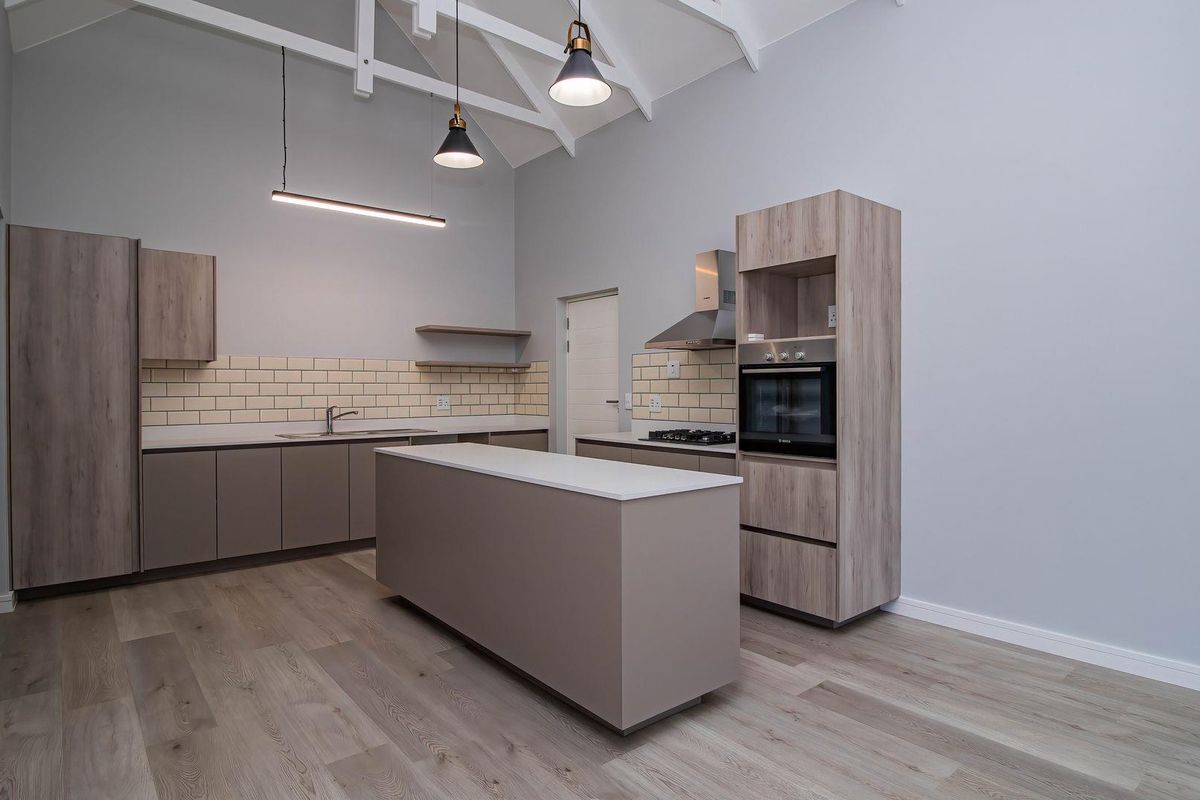 Modern kitchen featuring light wood-tone cabinetry, a central island, subway tile backsplash, built-in oven, and high vaulted ceilings with exposed trusses.