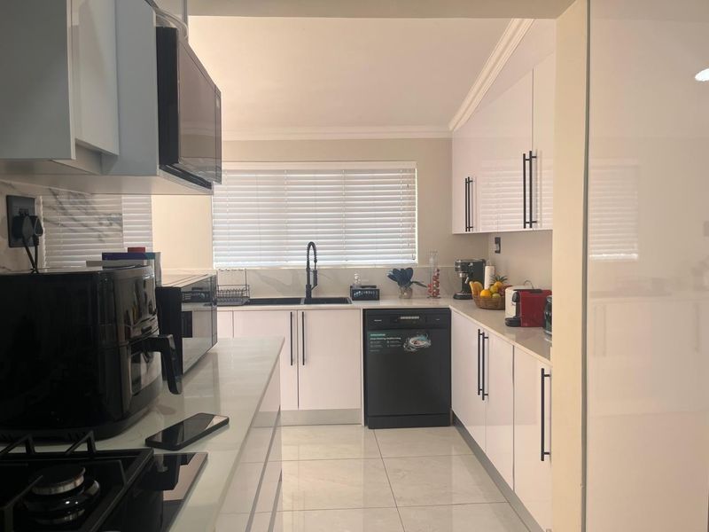 Modern kitchen featuring white high-gloss cabinetry, stone countertops, integrated dishwasher, gas hob, and built-in microwave with clean tiled flooring.