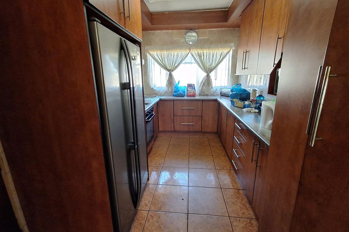 A functional galley-style kitchen featuring wood-finish cabinetry, tiled flooring, and integrated appliances, offering a practical layout for daily meal preparation.