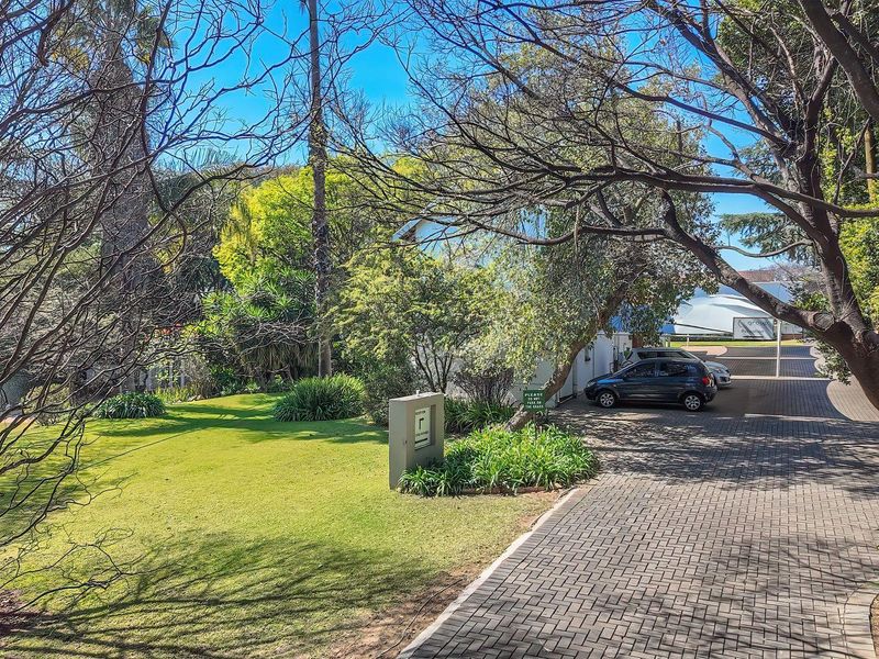 A well-maintained office property entrance featuring a paved driveway, lush landscaped garden, and clear signage.