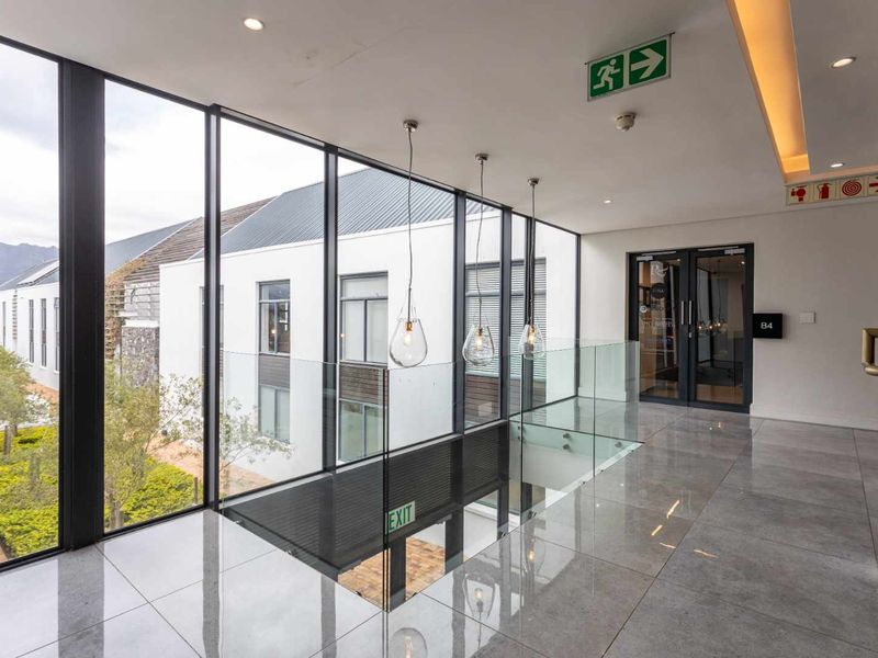 Modern commercial hallway featuring polished tile flooring, a glass balustrade, and floor-to-ceiling windows overlooking the exterior grounds.