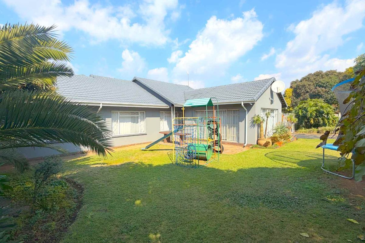 Rear view of the house featuring a tiled roof, paved patio area, and a spacious garden with established landscaping.