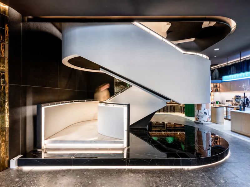 A modern, architecturally designed lobby featuring a striking sculptural staircase with integrated LED lighting and premium dark stone flooring.