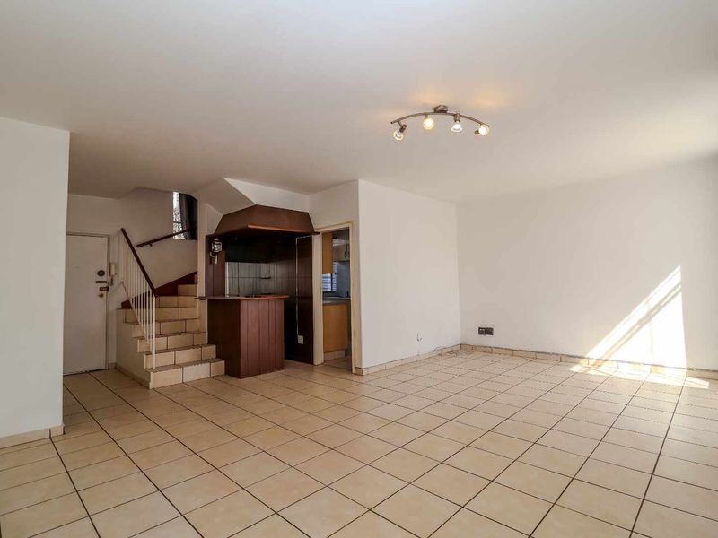 Spacious open-plan living area featuring tiled flooring, a built-in bar counter, and a staircase leading to the upper level.