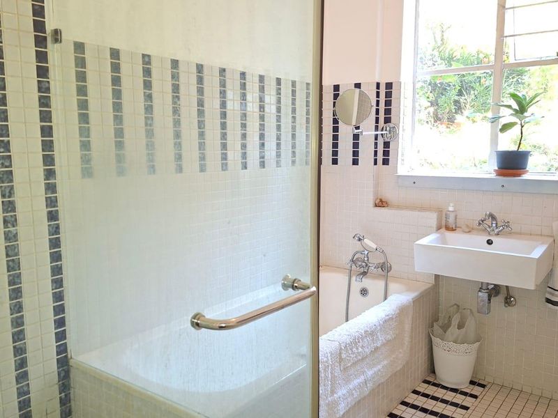 A functional bathroom featuring a built-in bathtub with a glass screen, wall-mounted basin, and mosaic tile finishes throughout.