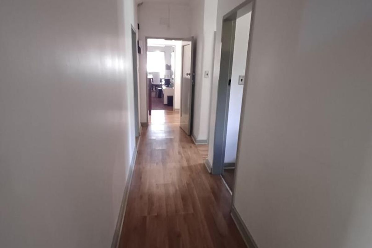 A clean, empty hallway featuring laminate wood flooring and neutral walls, providing access to multiple rooms within the home.
