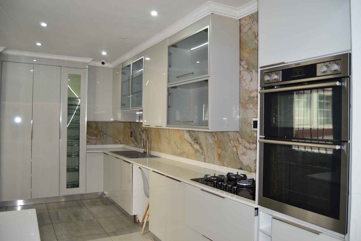 Modern kitchen featuring high-gloss cabinetry, stone-look backsplash, integrated double oven, gas hob, and sleek porcelain floor tiles.