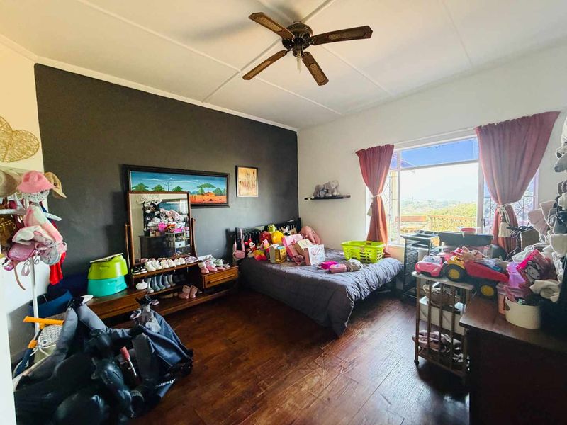 A bedroom featuring timber flooring, a ceiling fan, and a large window providing natural light and exterior views.