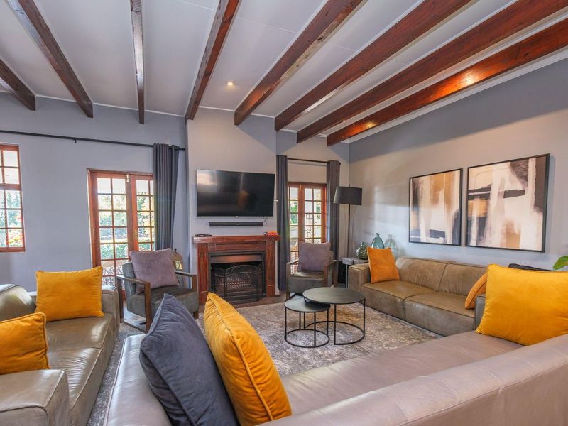 Spacious living room featuring exposed timber ceiling beams, a central fireplace with a wooden mantel, and double french doors leading to the exterior.