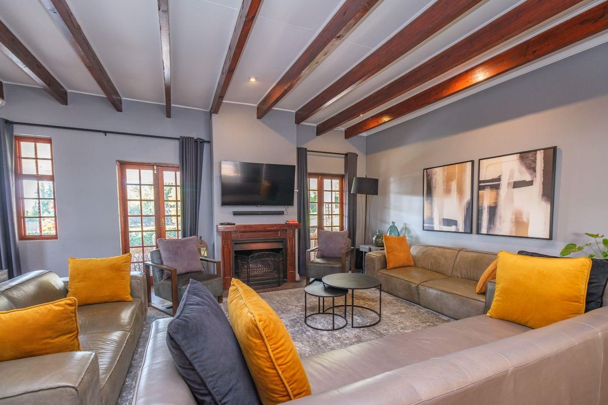 Spacious living room featuring exposed timber ceiling beams, a central fireplace with a wooden mantel, and double french doors leading to the exterior.