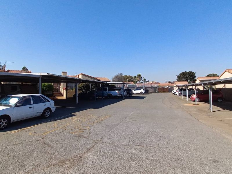 An outdoor parking area featuring multiple covered carport bays with asphalt surfacing within a residential townhouse complex.