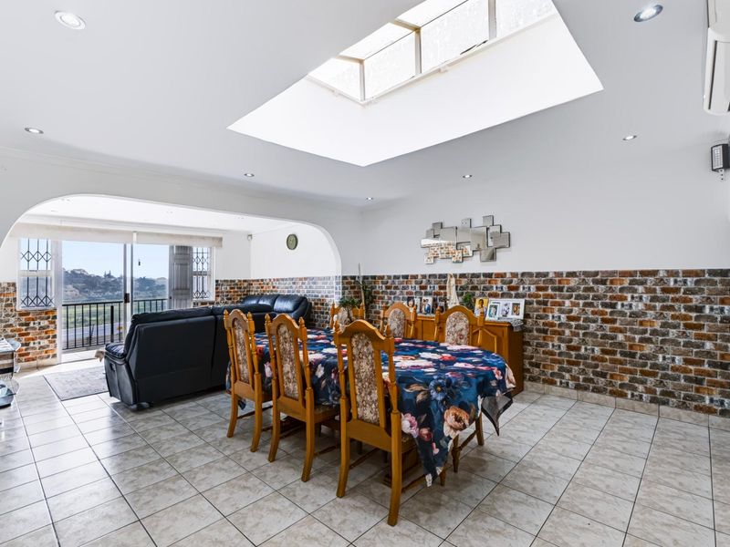 Spacious open-plan dining and living area featuring a large skylight, exposed brick accents, tiled flooring, and direct access to a balcony with scenic views.