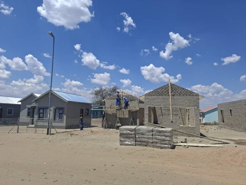 A construction site showing residential houses in various stages of development with exposed masonry and metal roofing.