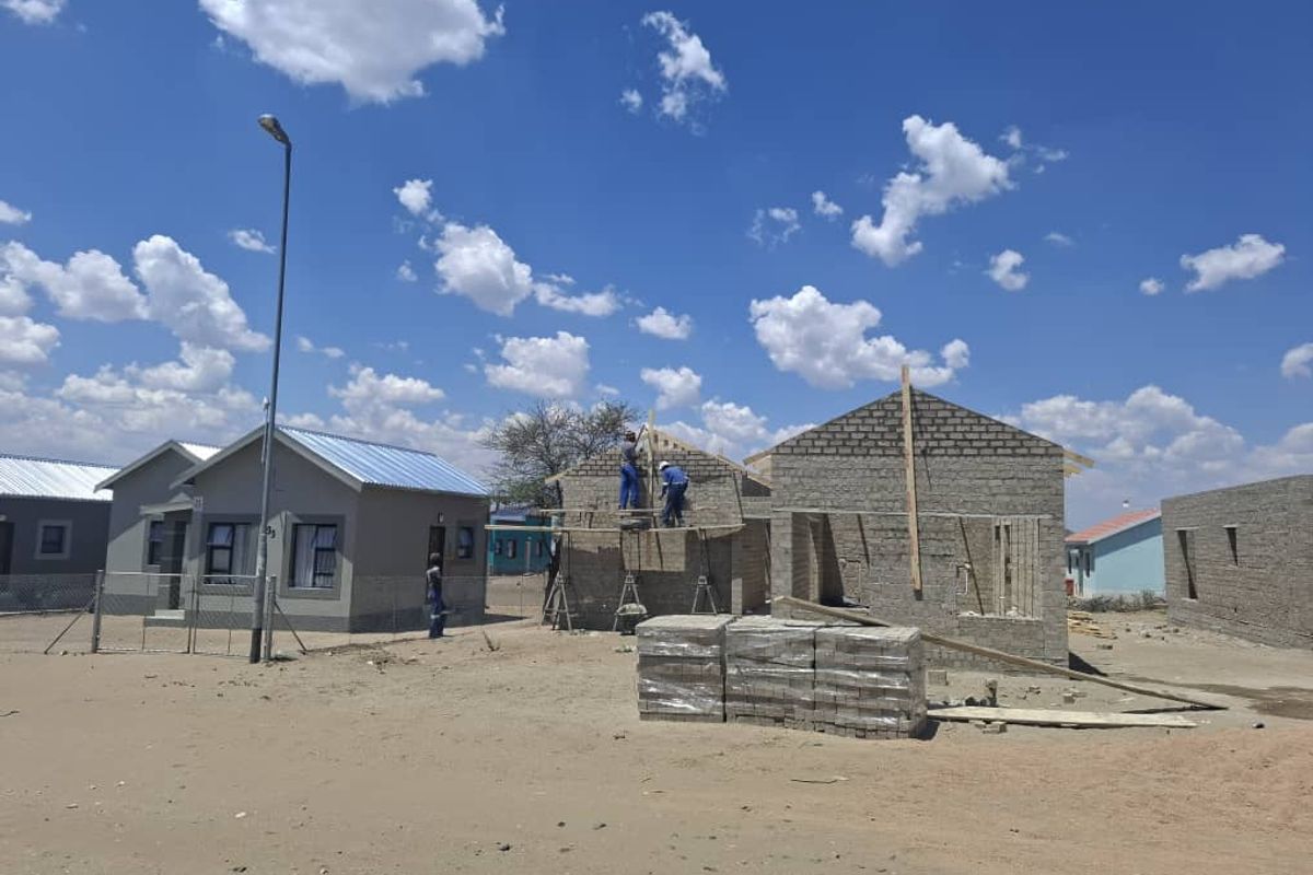 A construction site showing residential houses in various stages of development with exposed masonry and metal roofing.