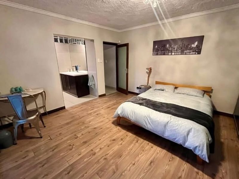 Spacious bedroom featuring laminate flooring, ceiling coving, and an integrated en-suite bathroom with a modern vanity unit.