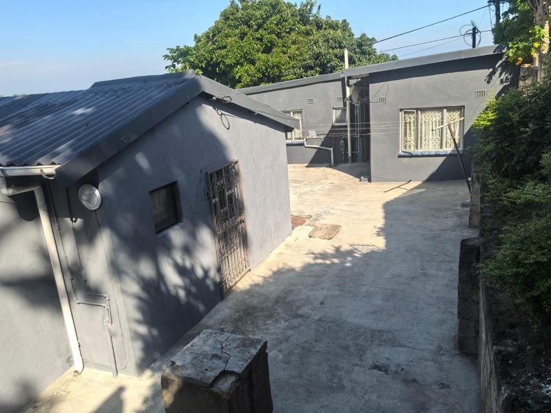 Rear exterior view of the property featuring concrete paving, security gates, and tiled roofing on the main structure and outbuilding.