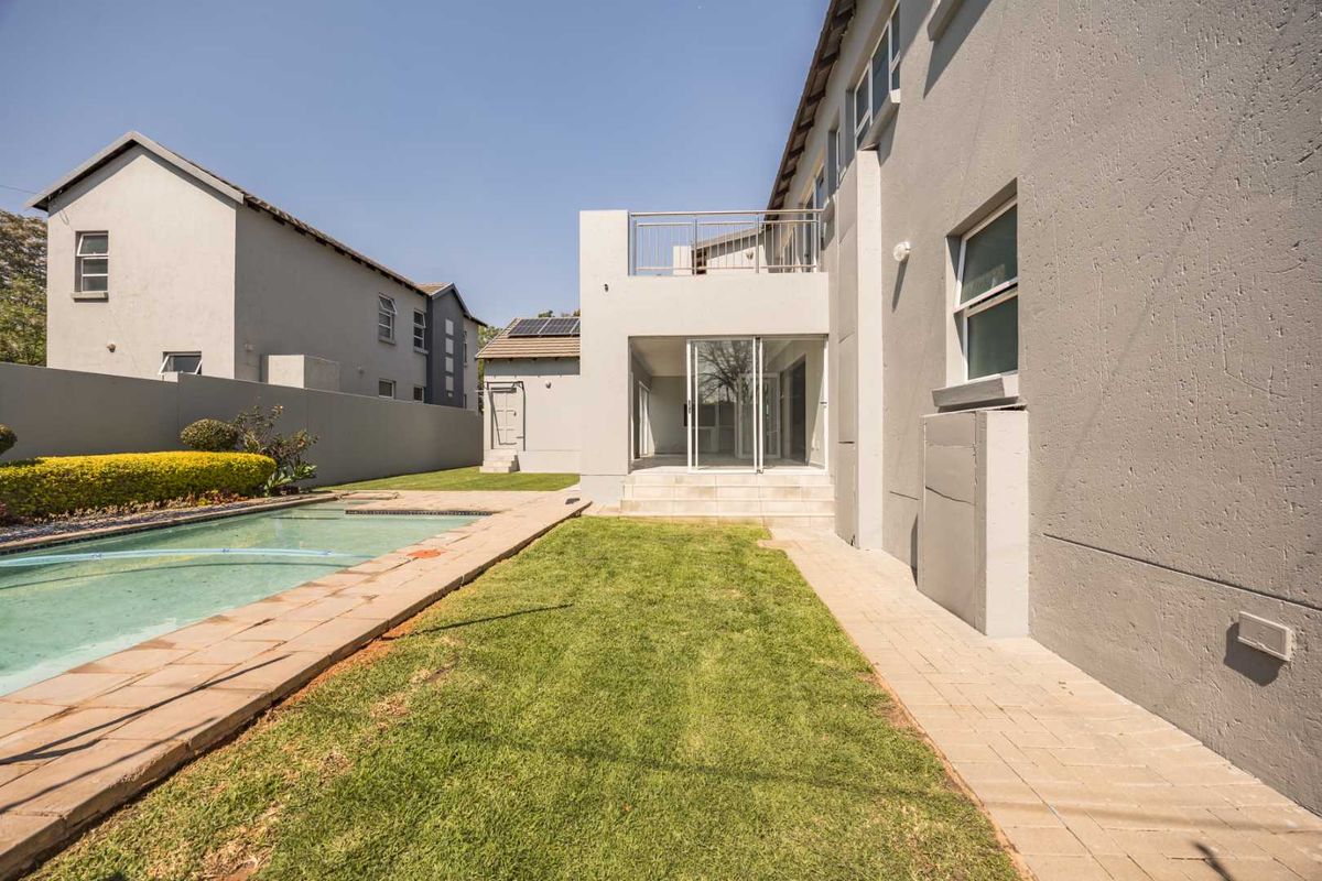 Rear exterior view featuring a swimming pool, paved surround, lawn area, and a balcony with metal railings attached to the main dwelling.