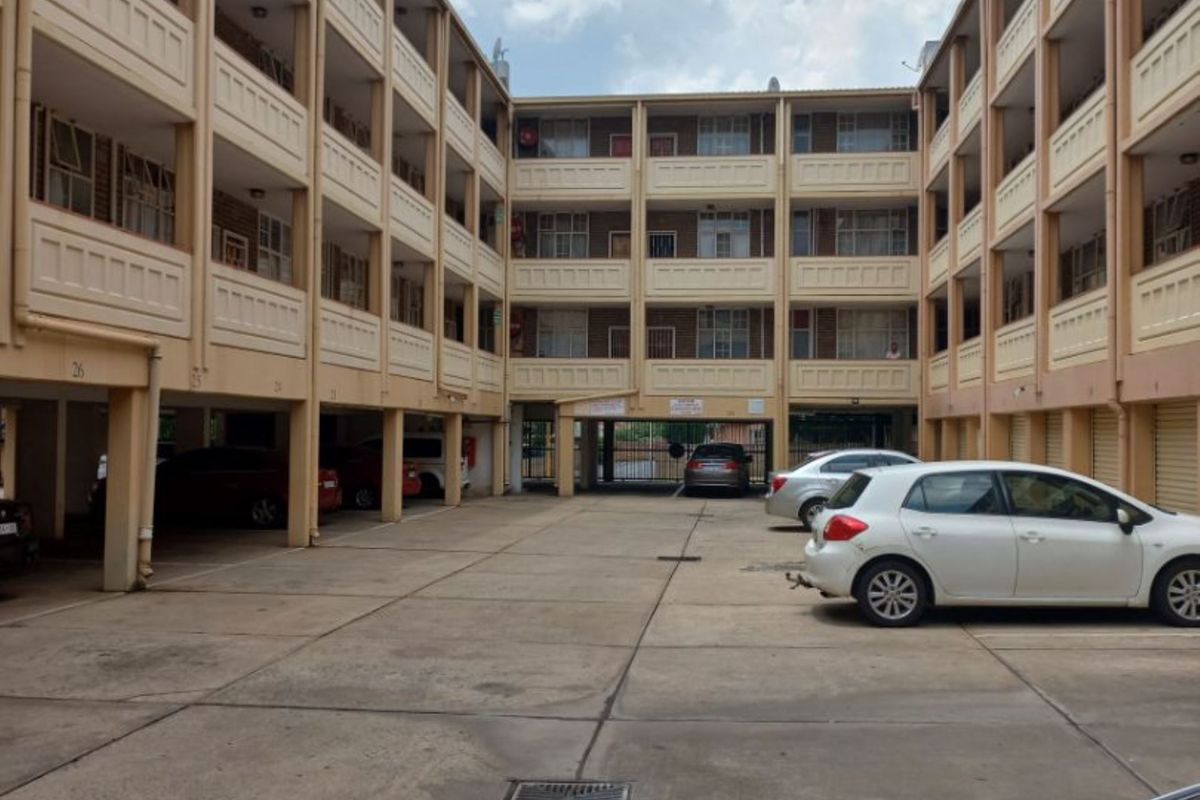 Exterior view of a multi-story apartment complex featuring covered ground-level parking bays and open-air walkways.