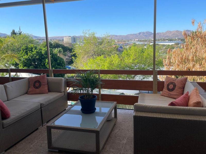 A covered balcony featuring a timber railing and tiled flooring, offering expansive views of the surrounding landscape and distant mountains.