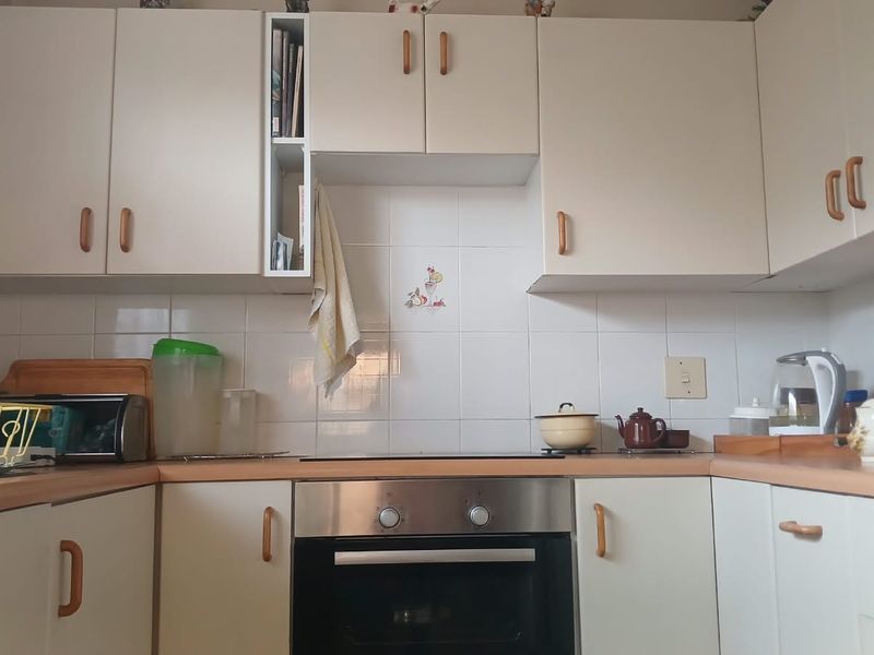 A functional kitchen featuring light-toned cabinetry, laminate countertops, a ceramic tile backsplash, and a built-in oven with an electric hob.