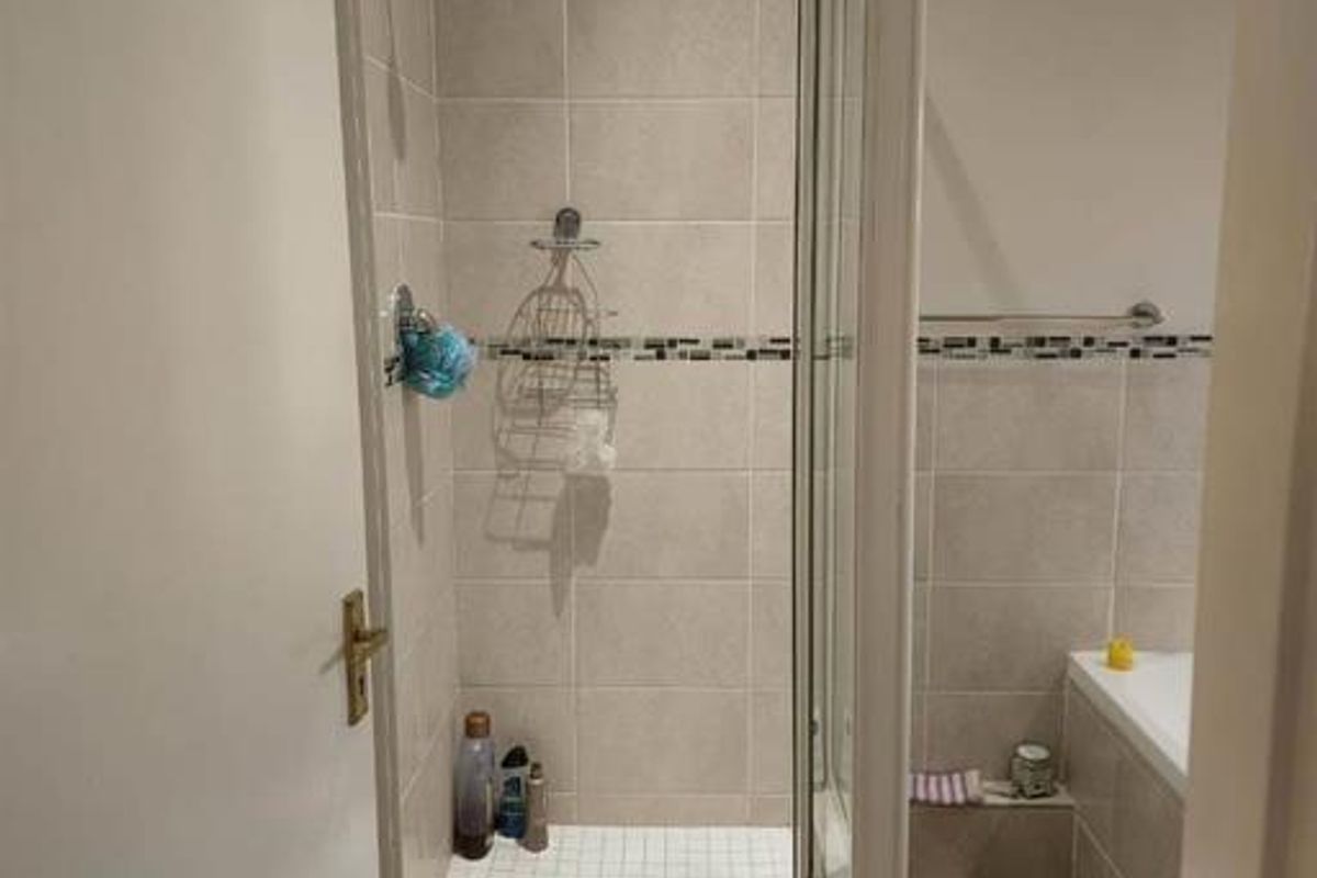 A functional bathroom featuring a tiled shower enclosure, a built-in bathtub, and neutral wall tiling with a decorative accent border.