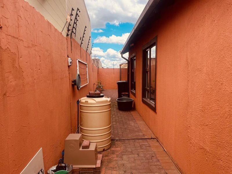 A narrow paved side passage featuring a water storage tank, electric fencing, and exterior wall access.