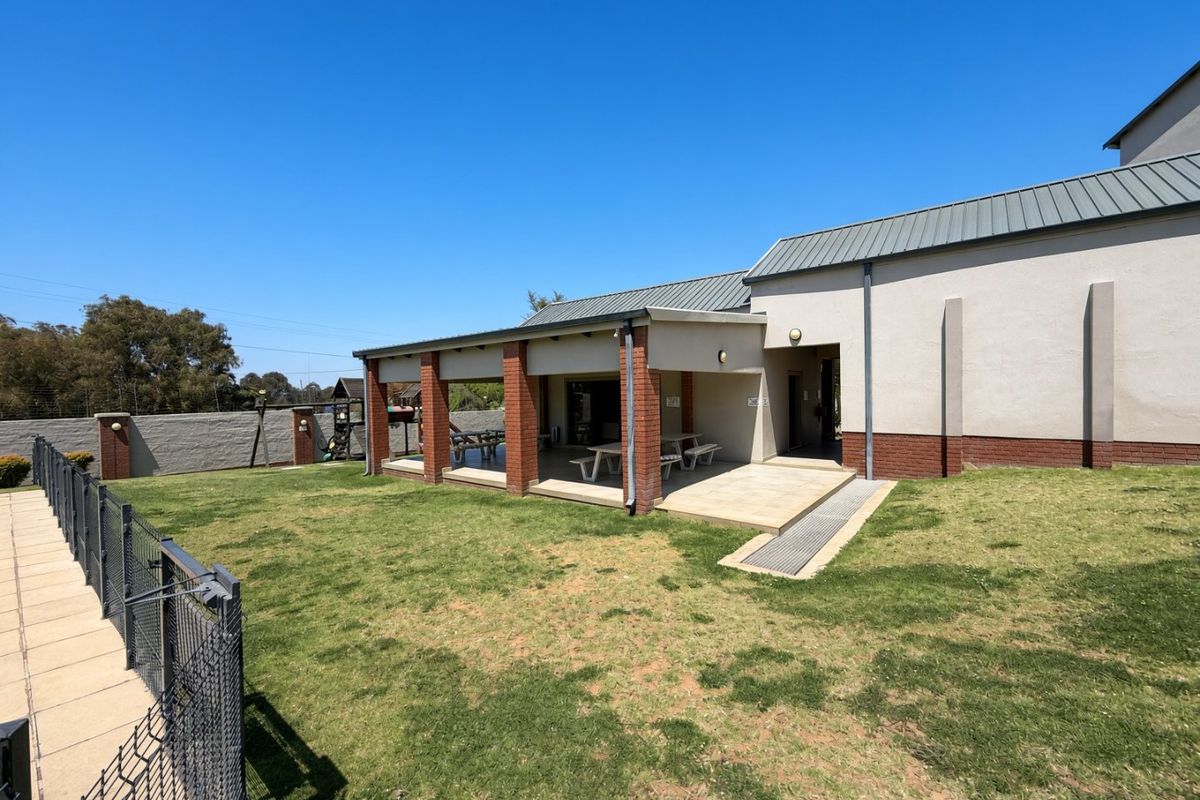 A spacious rear exterior area featuring a covered patio with brick pillars, concrete flooring, and a well-maintained lawn enclosed by perimeter fencing.