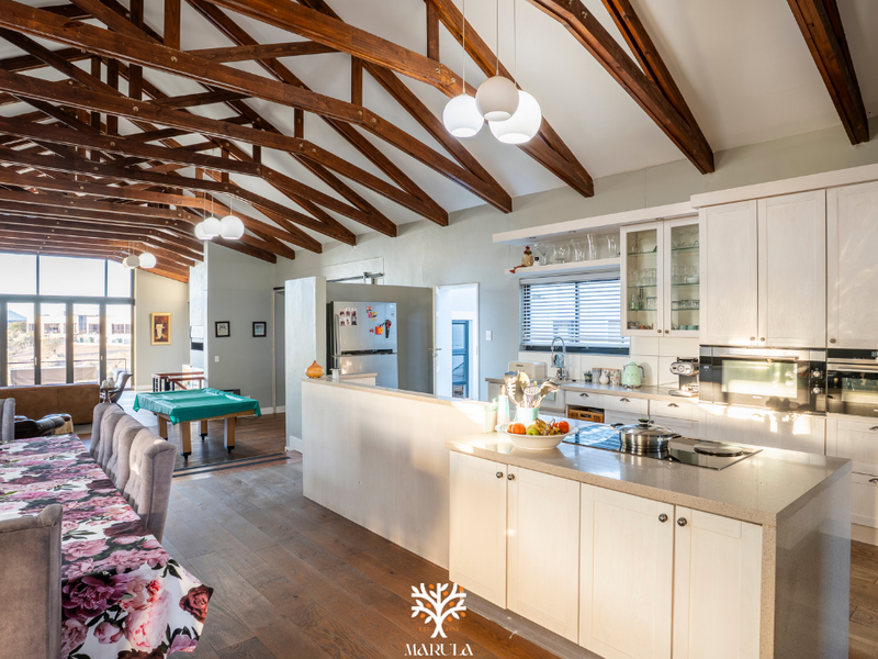 Spacious open-plan living and kitchen area featuring high vaulted ceilings with exposed timber trusses, a central kitchen island, and modern cabinetry.