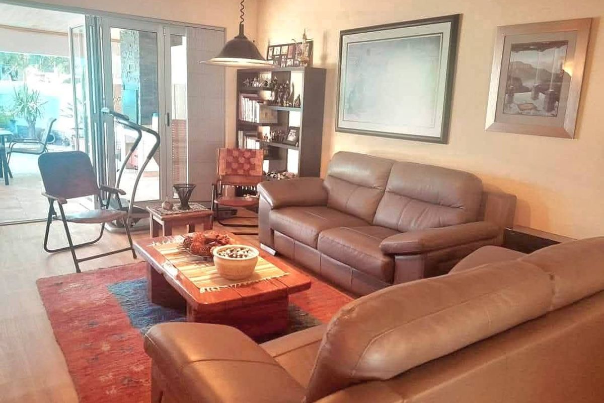 A comfortable living room featuring exposed timber ceiling beams and large aluminium stacker doors providing seamless access to the outdoor patio area.