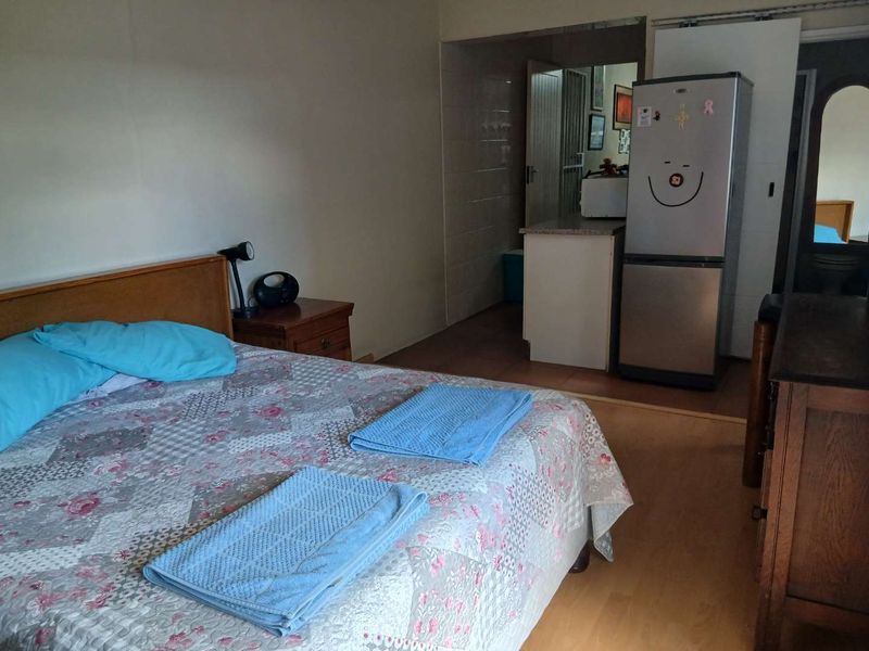 A bedroom featuring laminate flooring and an adjoining kitchenette area with tiled walls and a breakfast counter.