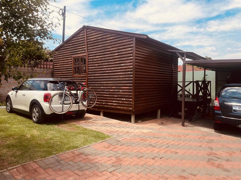 A detached log cabin structure featuring timber cladding and an attached carport, situated on a paved driveway with an adjacent timber deck.