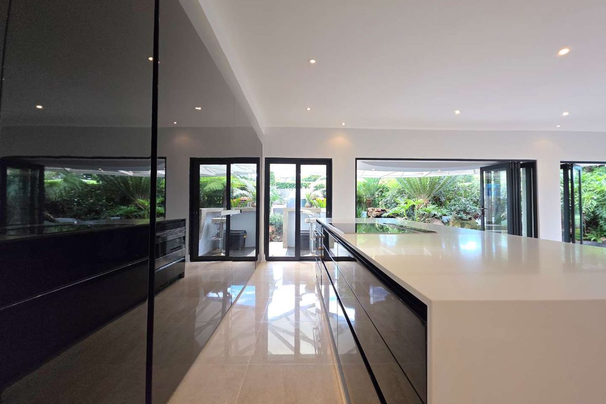 Modern kitchen featuring a large central island with stone countertops, high-gloss cabinetry, and seamless indoor-outdoor flow through expansive bi-fold doors.