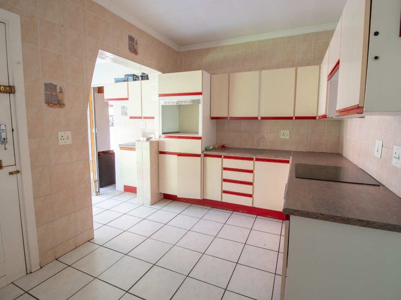 A dated kitchen featuring tiled walls and floors, built-in cabinetry, and an integrated electric cooktop, offering a functional space ready for modernization.
