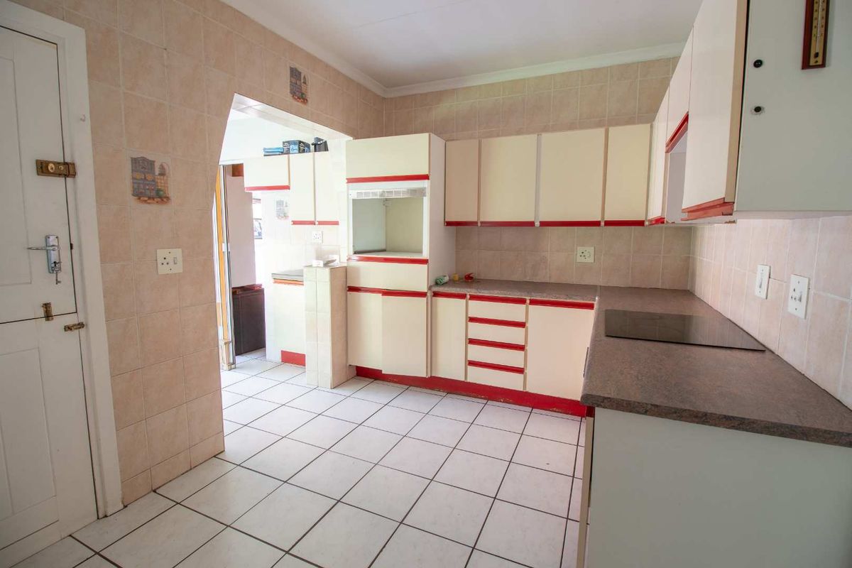 A dated kitchen featuring tiled walls and floors, built-in cabinetry, and an integrated electric cooktop, offering a functional space ready for modernization.