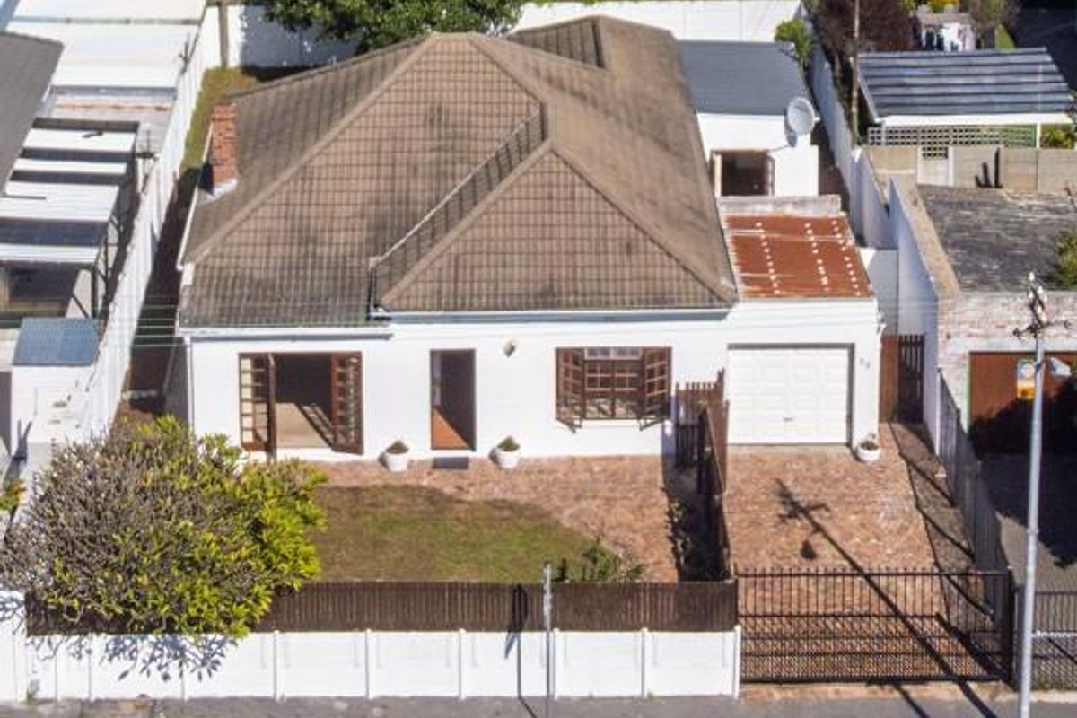 Aerial view of a detached house featuring a tiled roof, attached garage, paved driveway, and enclosed front garden with boundary wall and gate.